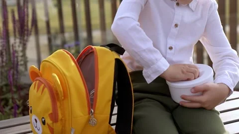 First grade school boy sits outside and opens vegetable lunch Stock Footage 244930402