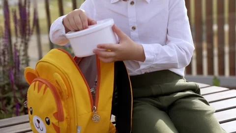 First grade school boy sits outside and opens vegetable lunch Stock Footage 244930416