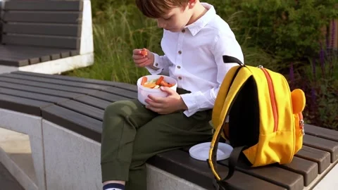 First grade school boy sits outside and opens vegetable lunch Stock Footage 246643780