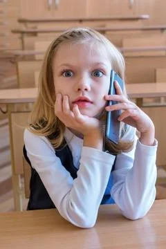 A first grade student at school speaks by phone. emotions of schoolgirls Stock Photos