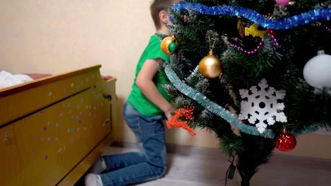A first-grader boy decorates an artificial Christmas tree at home Stock Footage 323702003