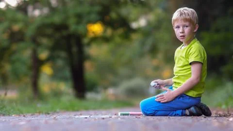 First-grader boy sitting on asphalt with chalk in hand and looking into the c Stock Photos