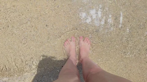 A first person perspective bare female feet in the foaming waves on a light sand Stock Footage 333989468