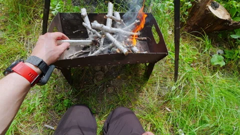 First-person POV of man igniting firewood in metal brazier for outdoor campfi Stock Footage 343550715