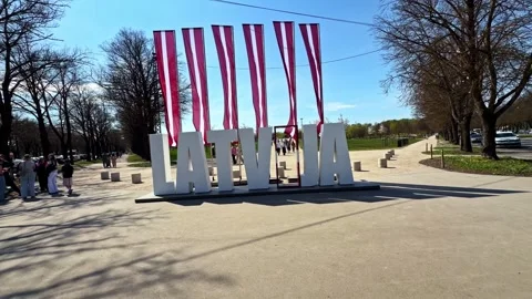 First Person Pov Walking Toward Large White Latvija Sign And Red Striped Flags Stock Footage 334691926