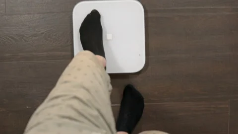 A first-person shot of a man getting on the scales. Weighing on scales. Male Stock Footage 154410957