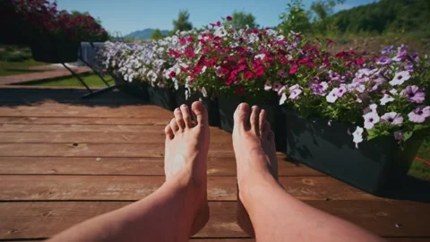 First-person view, bare feet on deck near flowering plants 库存影片 333514788