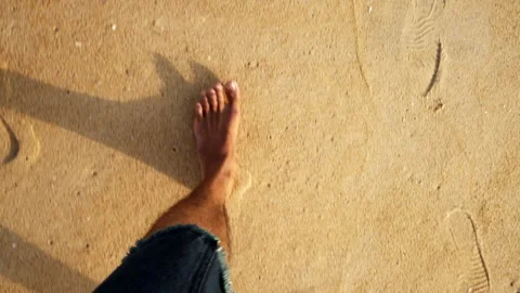 A first-person view of bare feet walking slowly across soft golden beach. Stockbeeldmateriaal 340959809