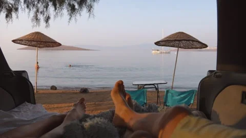 First person view of boy girl lying in camper van with table and chairs by sea Vidéo 257241217