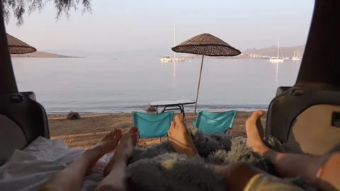 First person view of boy girl lying in camper van with table and chairs by sea Vidéo 257253175