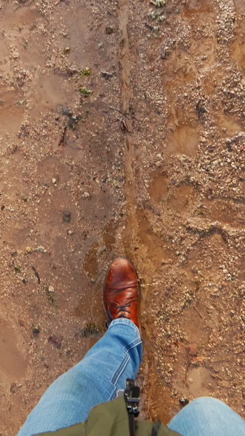First-person view of brown leather shoes walking through wet mud, capturing Stock Footage 333651492