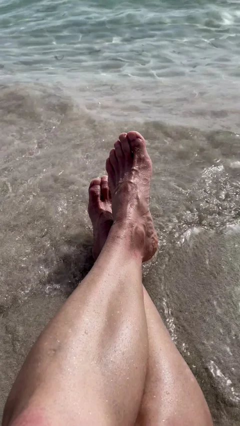 First person view of the crossed legs of a man sitting on the seashore Stock Footage 202250776