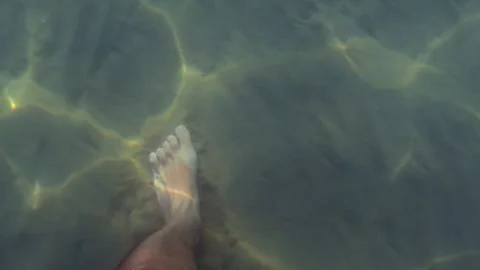 First-person view of man walking underwater on sandy seabed with sunlight Stock Footage 279899135
