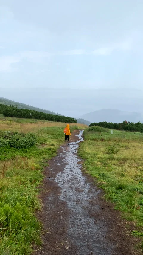 First person view walking by wet mountain tail woman in yellow raincoat ahead Stock Footage 219305452