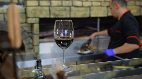 The first plan is a glass of wine, background Chef puts prepared meat on the Stock-Footage 104147403