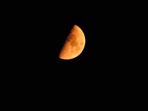 A first-quarter or half moon glowing in a vibrant orange hue against a dark Stock Photos