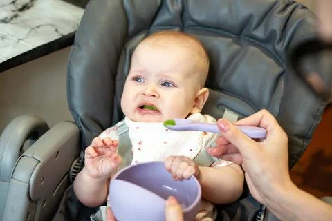 First solid food introduction for a baby with a funny facial expression Stock Photos