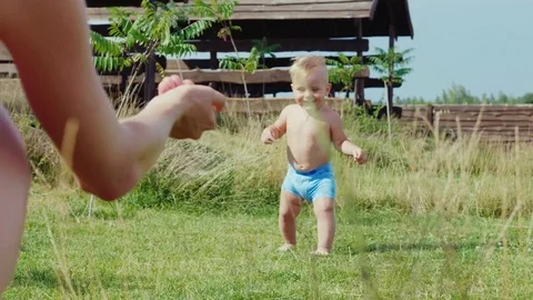 The first steps of the baby. The boy of 1 year uncertainly goes to mum. Stock Footage 78856432
