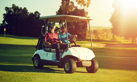 Off to the first tee. two golfers riding in a cart on a golf course. Stock Photos