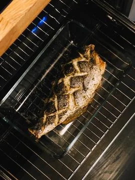 Fish baking with aromatic herbs and spices in glass container inside oven Stock Photos