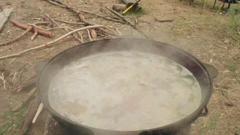 Fish is boiled in black pot on fire and man removes foam from broth. Cooking Stock Footage 144454192