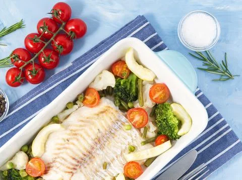 Fish cod baked in blue oven with vegetables - broccoli, tomatoes. Healthy d.. Stock Photos
