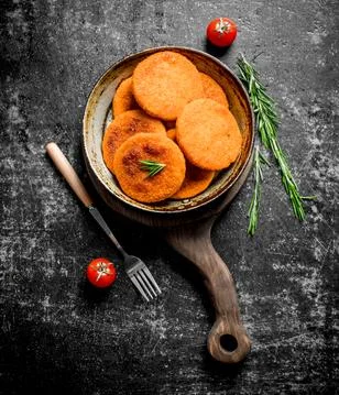 Fish cutlets in pan with fork and rosemary. Stock Photos
