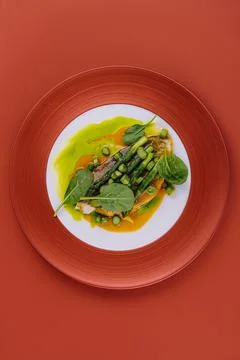 Fish dish - fried cod fillet with asparagus and basil served on red plate Stock Photos