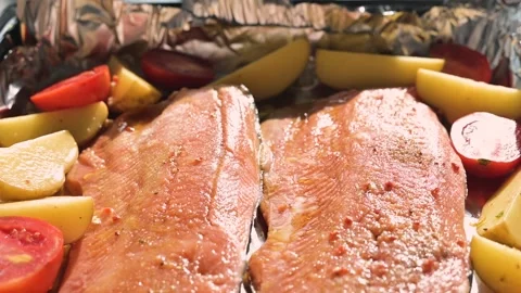 Fish fillets are placed in a baking dish surrounded by slices of potato, tomato. Видео 344667235