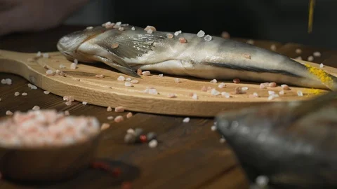Fish lying on cutting board are sprinkled with seasoning and salt for smoking Stock Footage 94586199