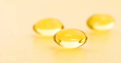 Fish oil supplement capsules on gold background. Cosmetics, omega 3 golden bu Stock Photos