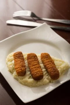 Fish sticks served with mashed potatoed on the white plate with silverware in Stock Photos