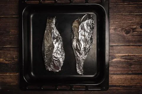 Fish wrapped in foil on a baking sheet and on a wooden table. Cooking fish in Stock Photos