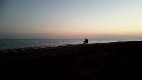 Fisherman on beach at dusk panning left and flying right  Stock Footage 252015845