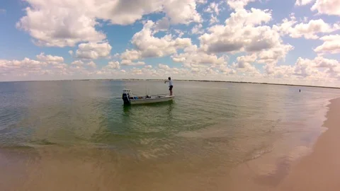 Fisherman casting from boat just off beach, waves gently lapping on shore Stock Footage 80561799