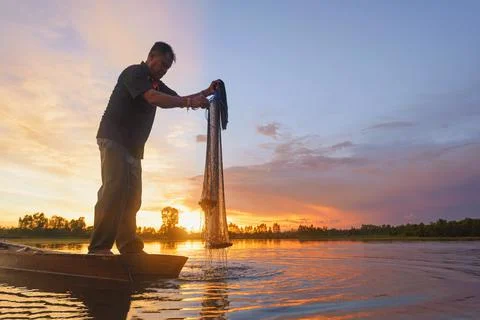Fisherman casting his net on during sunrise.Silhouette Asian fisherman on woo Stock Photos