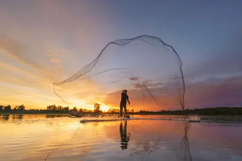 Fisherman casting his net on during sunrise.Silhouette Asian fisherman on woo Stock Photos