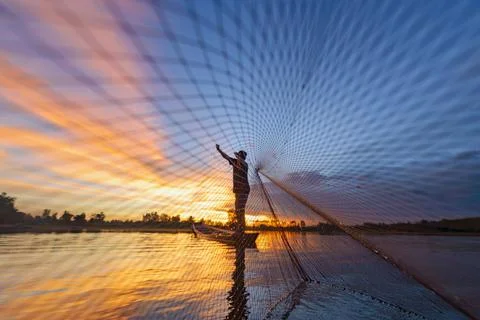 Fisherman casting his net on during sunrise.Silhouette Asian fisherman on woo Stock Photos