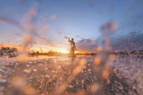 Fisherman casting his net on during sunrise.Silhouette Asian fisherman on woo Stock Photos