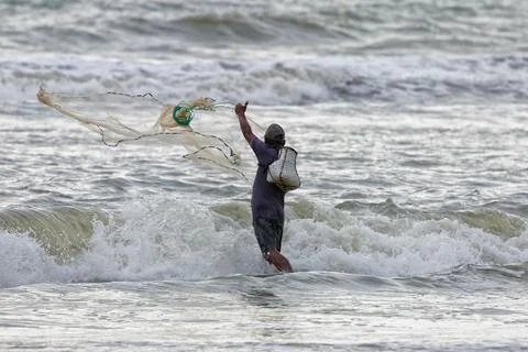 Fisherman casting net in ocean waves during traditional coastal fishing. Stock Photos