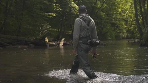 Fisherman crossing river with spinning rod in his hands. Trout fishing. Stock Footage 242446953