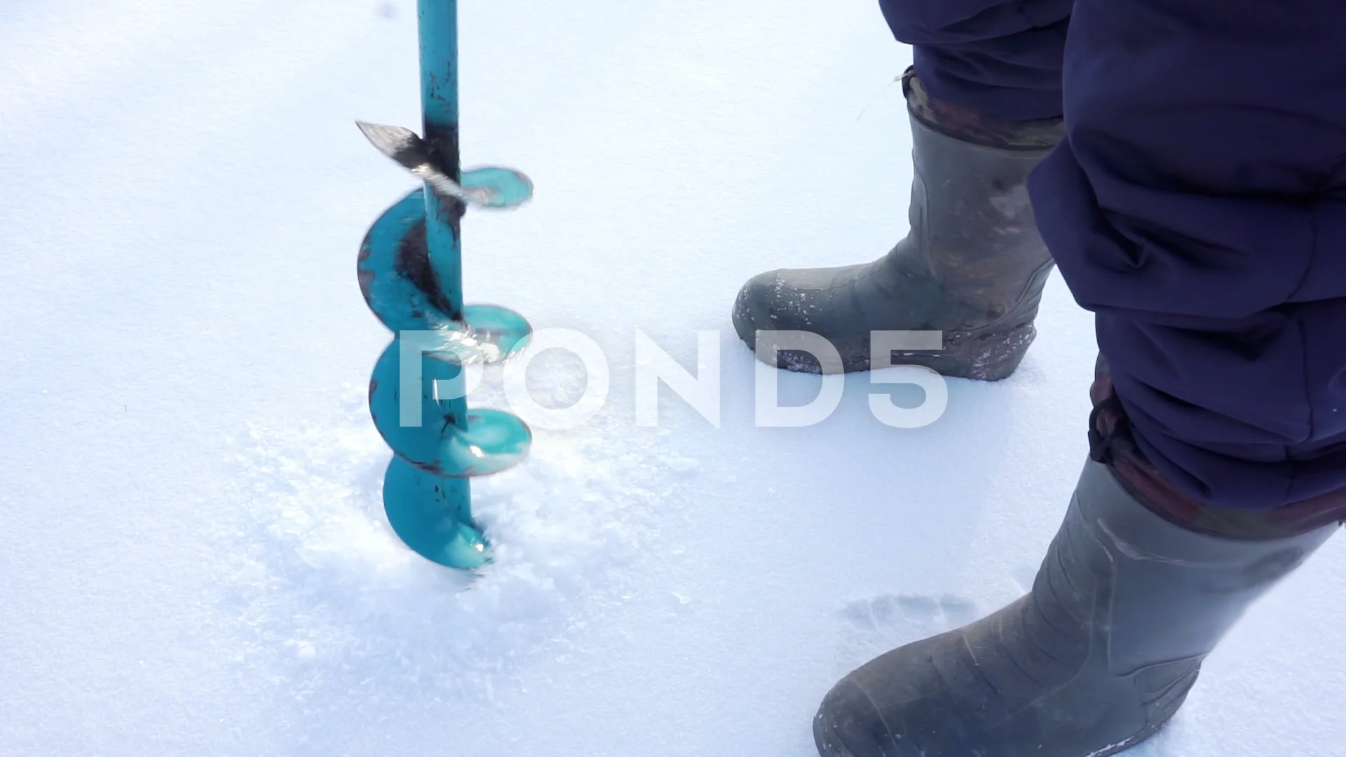 An ice fisherman using a hand auger to drill a hole on a frozen