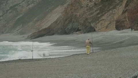 Fisherman on pebble beach with waves in slow motion Stock Footage 297791653