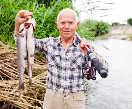 Fisherman posing with catch at riverside Stock-Fotos