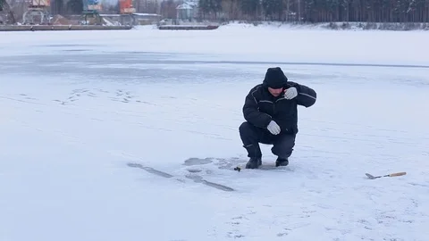 Fisherman prepare hook with bait and prepare for ice fishing on frozen river Stock Footage 99621605