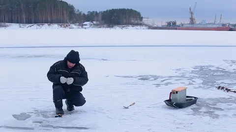 Fisherman prepare hook with bait and prepare for ice fishing on frozen river Stock Footage 99621640