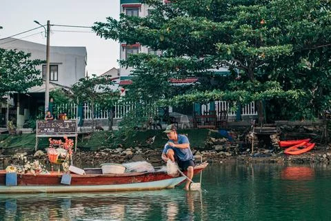 Fisherman preparing a fishing net while sitting in a traditional wooden boat on Foto stock