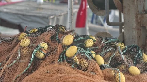 Fisherman is Repairing Fishnets on Fishing Boat in Dock Stock