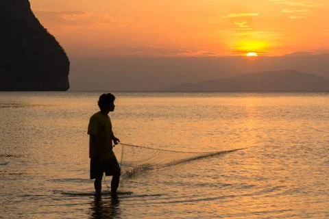 A fisherman pulls in his net at sunset on Rajamangala beach in Trang province Foto stock