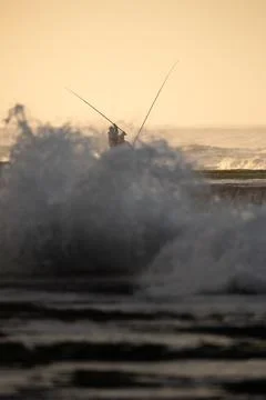 Fisherman on Rock with Dramatic Ocean Wave Splash Fotos de archivo